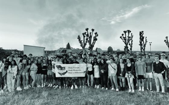 Photo Of Wiesbaden Community Spouses’ Club holding sign. SIgn reads “Make friends. Make memories. Make a difference.”