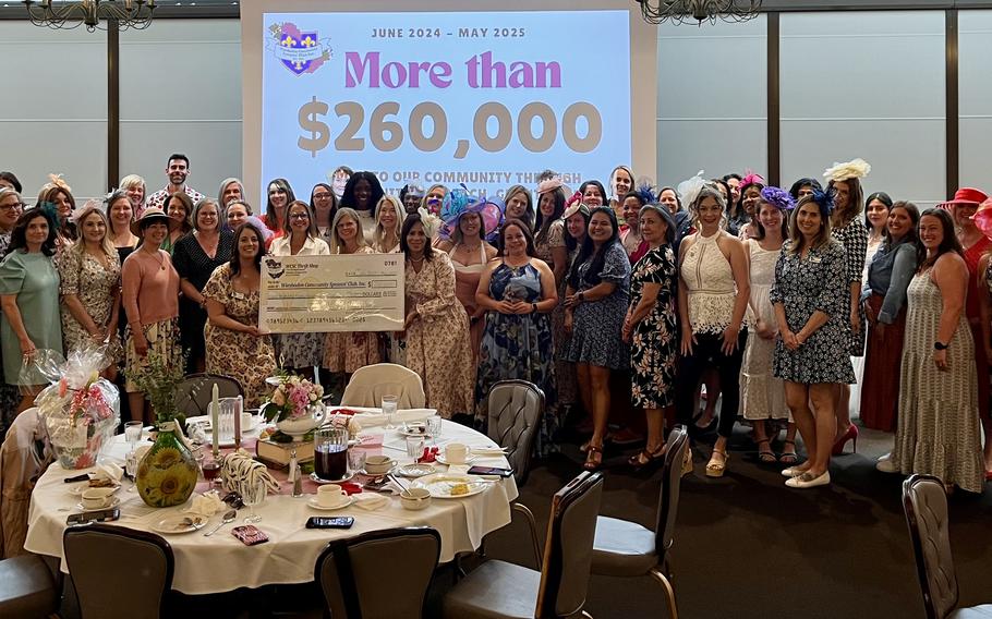 Wiesbaden Community Spouses’ Club luncheon, May 21, 2025 with participants standing behind a circular table and infront of a digital sign reading “More than$260,000”