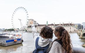 Two young teenagers stand in front of the Thames to indicate the London Eye