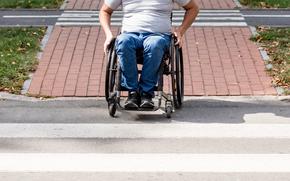 Man in wheelchair preparing to cross the road on pedestrian crossing on sunny day