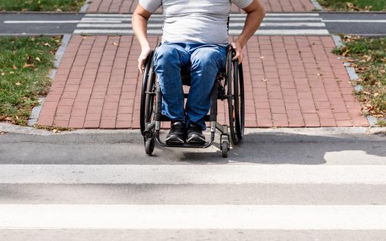 Photo Of Man in wheelchair preparing to cross the road on pedestrian crossing on sunny day