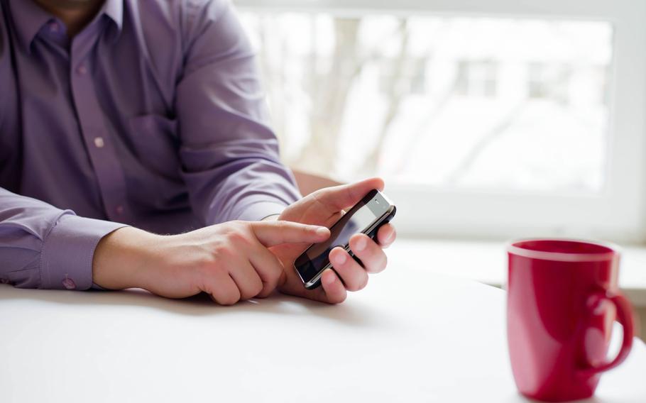 Man sitting at table, partially off-screen, typing on cell phone.