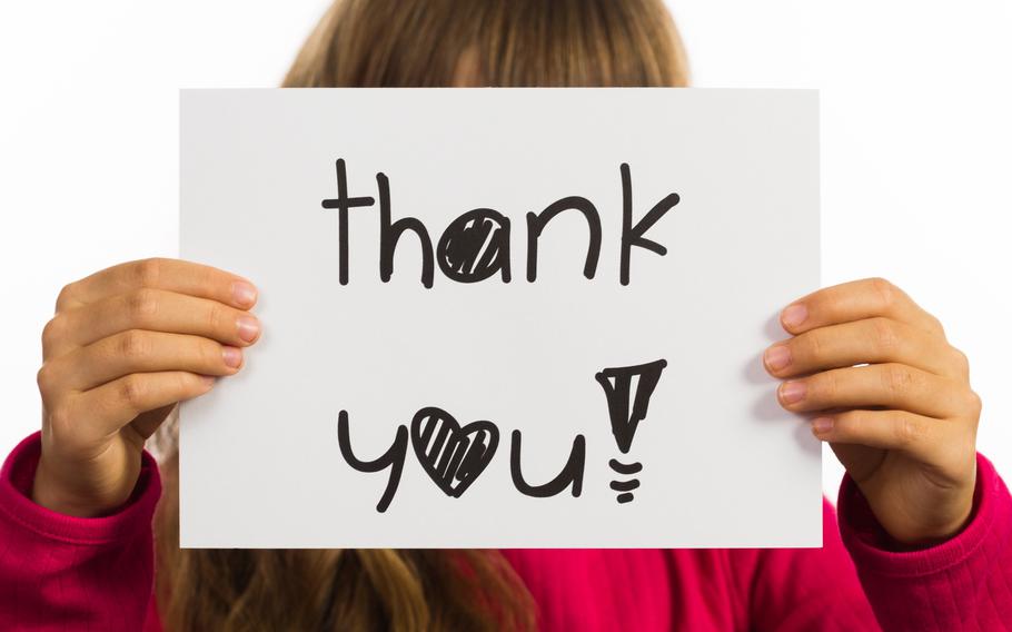 Studio shot of child holding a Thank You sign made of white paper with handwriting.