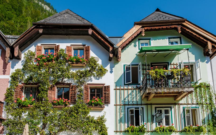 Quaint buildings in Hallstatt showcase intricate architecture and colorful balconies. Lush greenery and flower-filled window boxes create a picturesque ambiance under a clear blue sky.