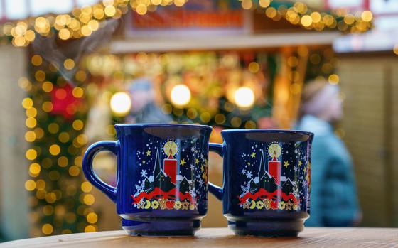 Two dark blue Christmas mugs with bright red candles on them against the back drop of a lit-up market stall. 