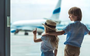 Back view of girl pointing away while looking out window together with brother in airport