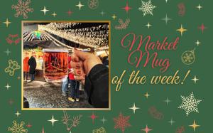 A glass Christmas market mug filled with red gluwein being held against a backdrop of twinkly lights. 