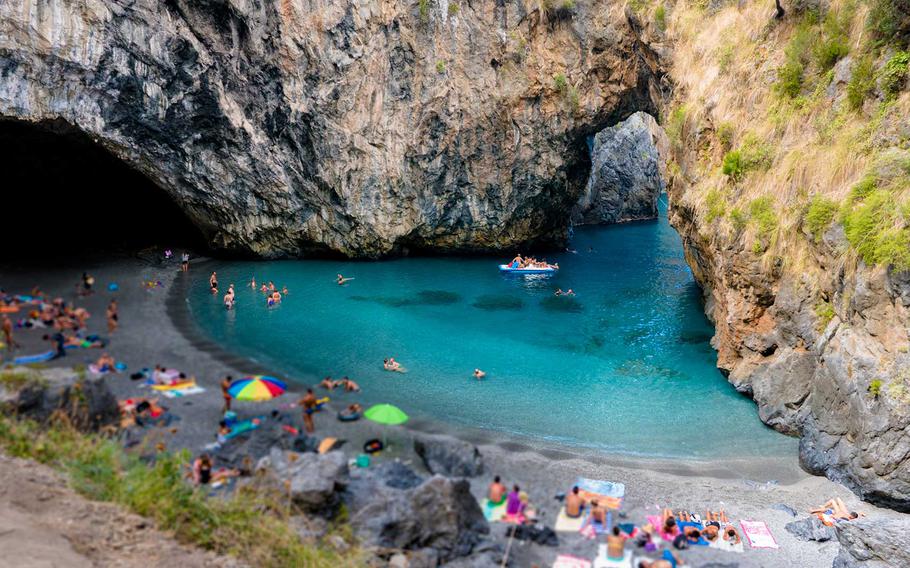 
A beautiful cove at Grotta delle Ninfe, Italy, with crystal-clear turquoise waters, dramatic rock formations, and beachgoers enjoying the serene and secluded spot.