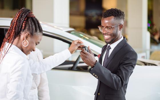 Sales situation in car dealership, young african couple gets the key for the new car