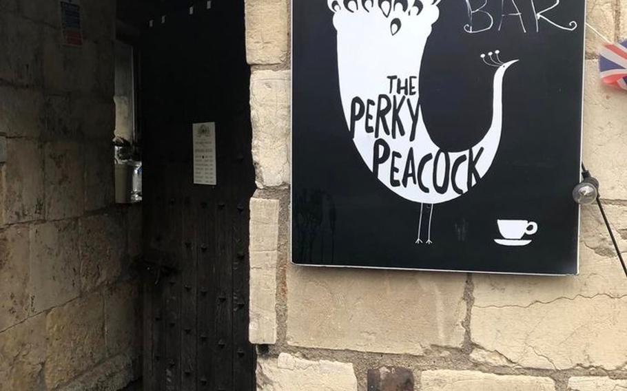Entrance to the Perky Peacock: a cafe inside of a castle tower. The black and white sign for the cafe sits perched on the beige castle wall. 