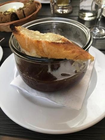 French onion soup | Brown broth in a clear bowl topped with a slice of toasted bread with melted cheese