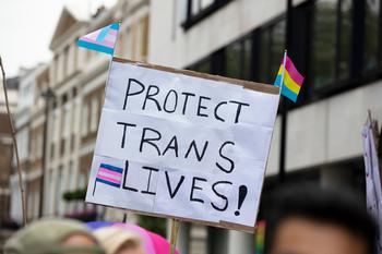 A person holding a sign reading protect trans lives banner