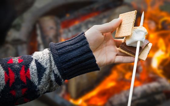 Closeup of Hands Building Smore with Roasted Marshmallow and Chocolate At Campfire Outdoors