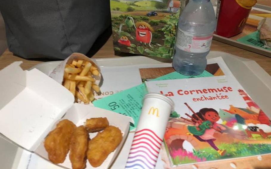 Happy meal on a tray with an open box of four McNuggets, a small books, a small bag of French fries and a frozen McDonald’s popsicle. 