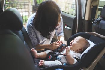 Mother fastening safety belt to her baby boy in the car seat