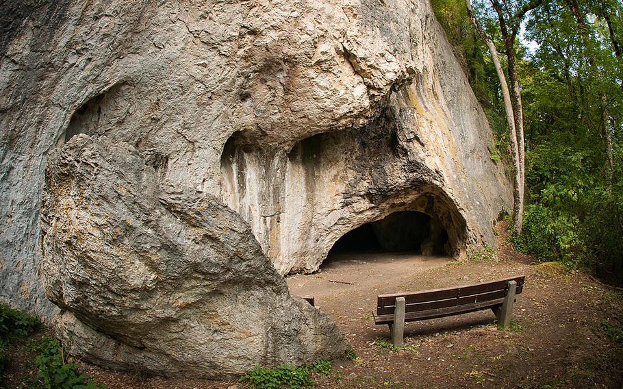 A view of the outside of a cave with an empty bench nearby