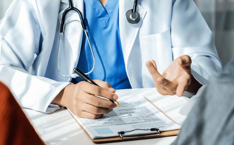 Photo Of Husband and wife support each other through the doctor appointment facing away from camera at the doctor’s desk