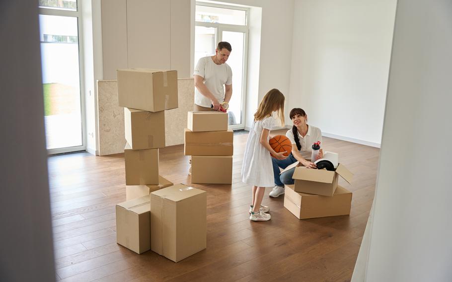 Family unpacking things in the living room of their new house, a girl takes a basketball out of a box