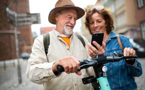 Close up of happy senior couple tourists scanning code to rent a scooter together outdoors in town