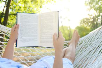 Person reading a book facing away from the camera on a hammock on a sunny day