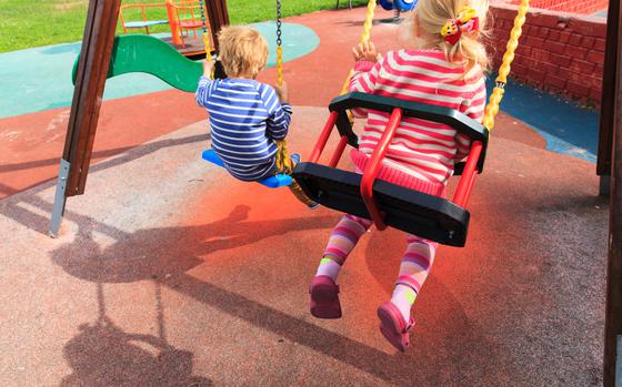 little girl and boy having fun on swings at playground outdoors