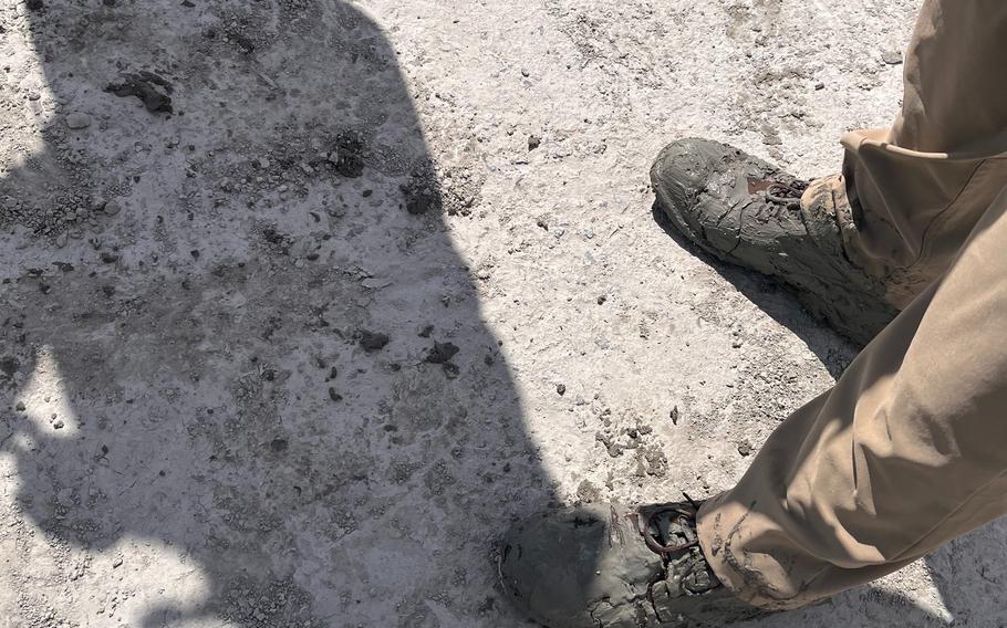 A picture focusing on a pair of utility boots caked in grey, sandy muck. 