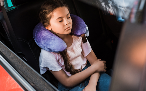 Photo Of A young child sleeping in a car seat wearing a purple neck pillow
