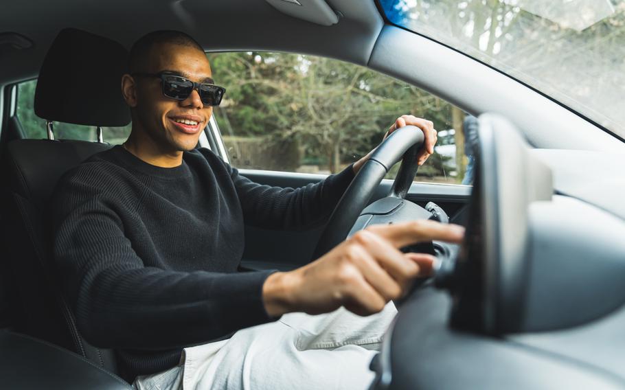 Young adult guy sitting on drivers seat and changing radio settings in the car