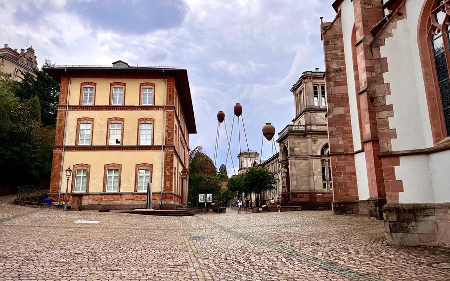 street view of a yellow and brown historic building sitting on cobblestones. 3 brown, round structures stand int he distance like water towers. 