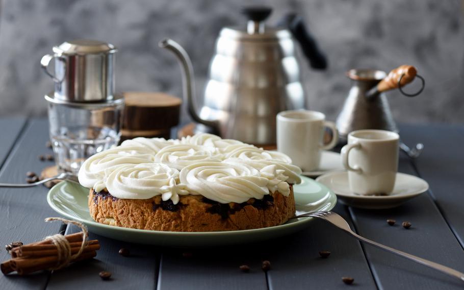 Homemade cake with white rose shaped icing served with coffee on dark grey  background copy space. Still life with natural lighting