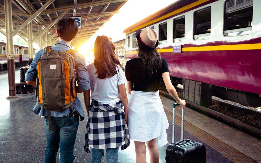 Three people looking away from the camera and carrying luggage next to a stopped train