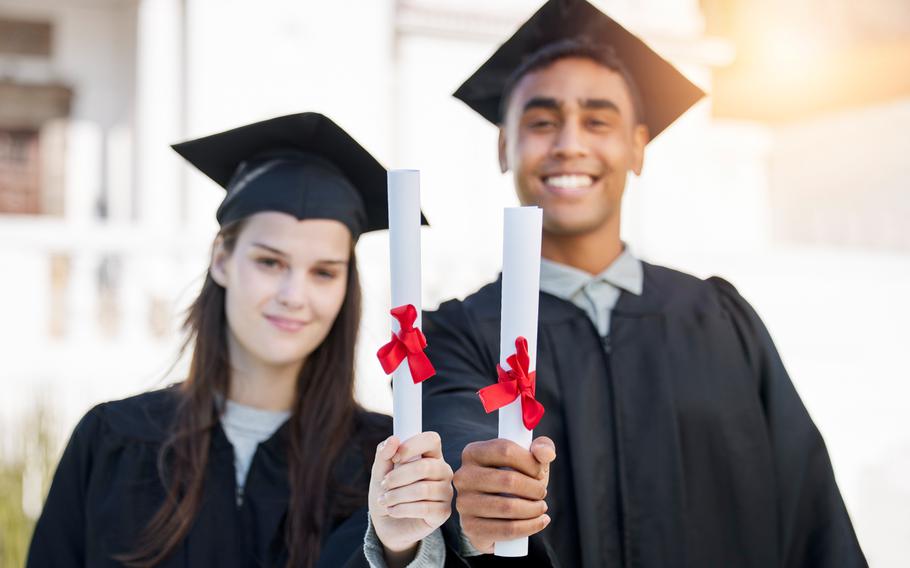 Two students holding certificates wearing graduation robes and hats