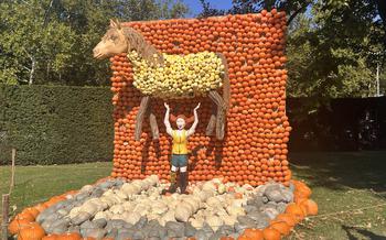 a girl sculpted out of bright gourds with orange braids holding a horse above her head