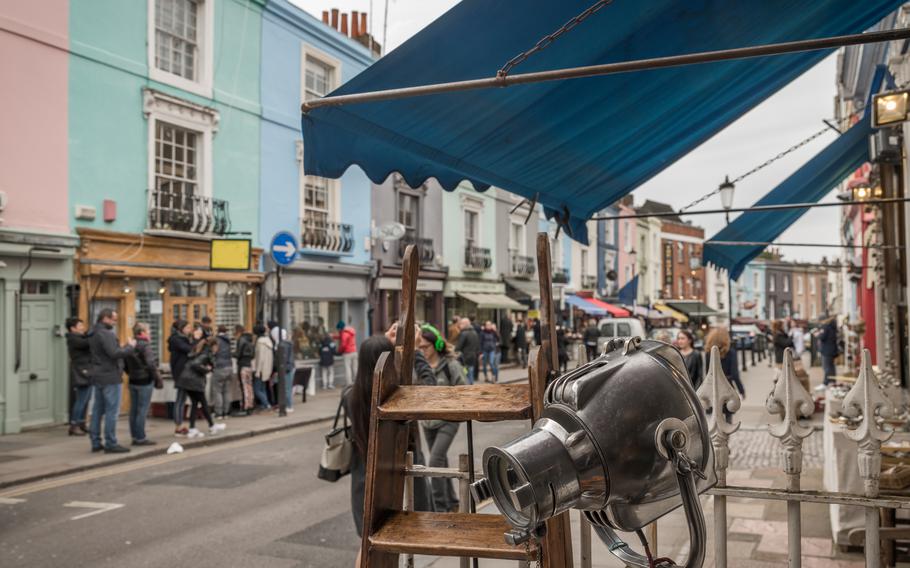 A canopy hangs over some antiques at a street market with colorful buildings at that back.