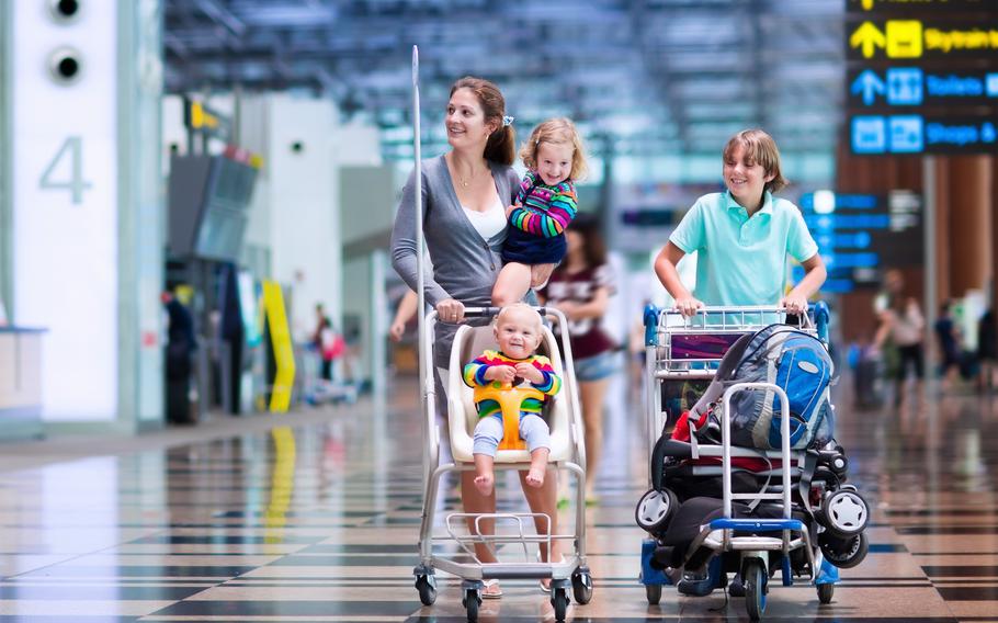 Family travels. Parent with children at international airport with luggage in a cart. Mother holding baby toddler girl and boy flying by airplane. 