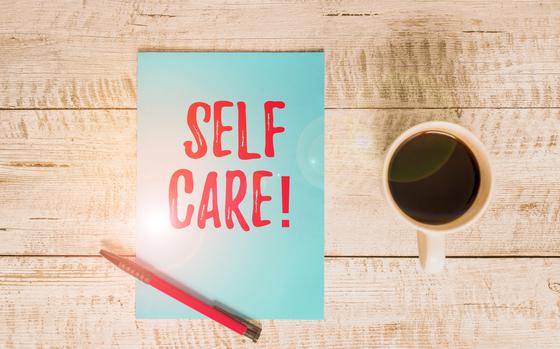 Words “SELF CARE” written in red on light blue paper next to a cup of coffee