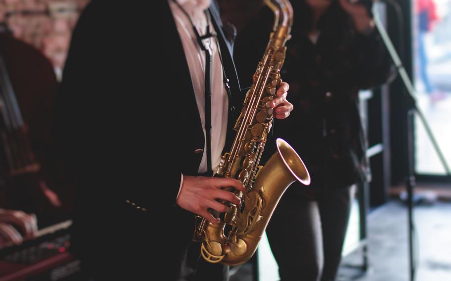 A saxophone sax player with vocalist and musical band during jazz orchestra show performing music on a stage in the lights.