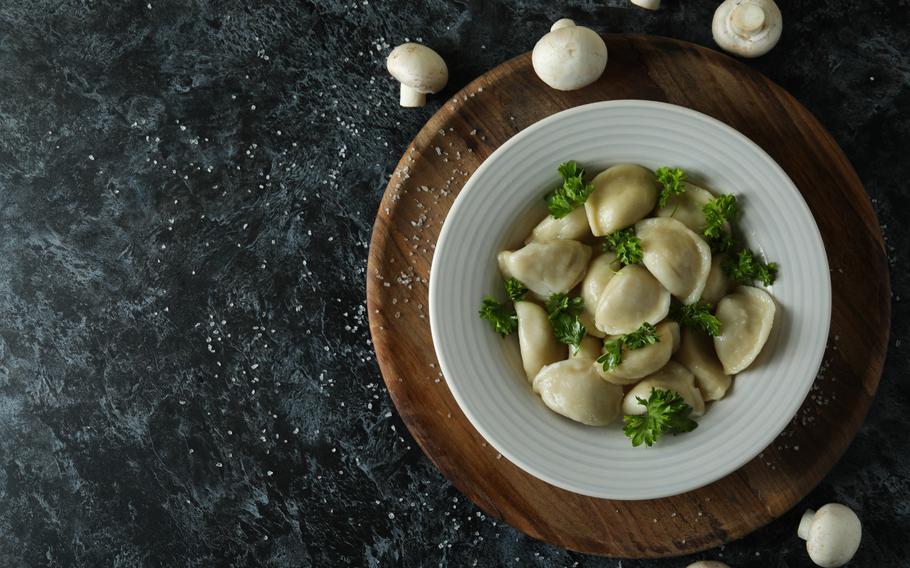 Pierogi in a white bowl with white mushrooms around bowl.