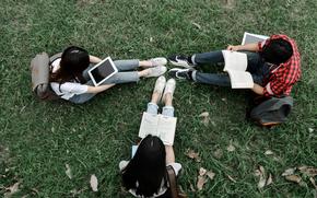  Students are reading books and tablets on the green grass.