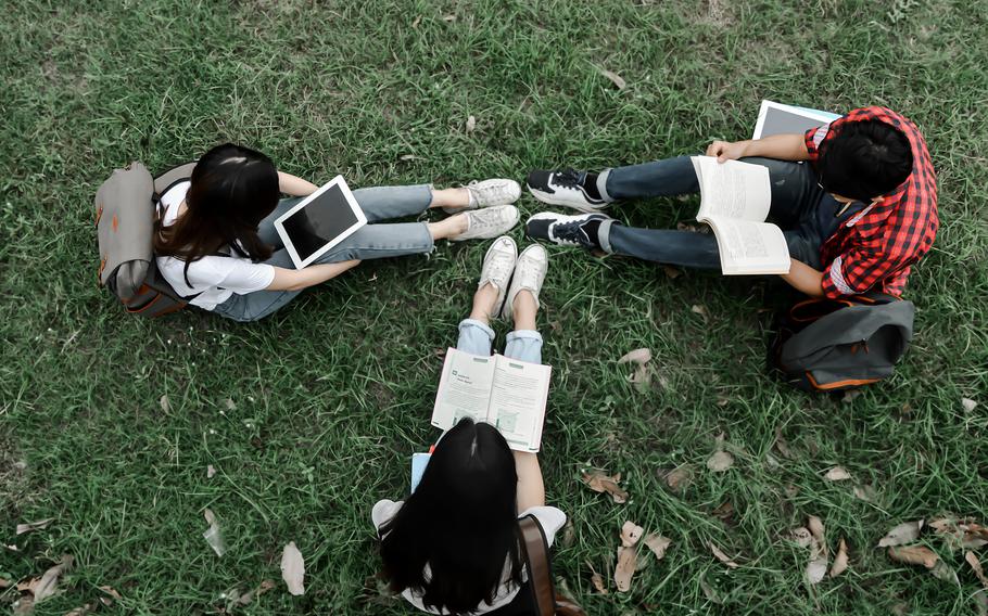  Students are reading books and tablets on the green grass.