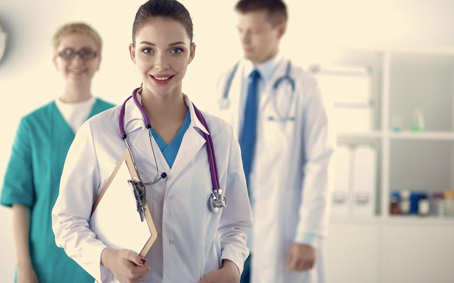 Female doctor with a stethoscope around her neck, standing in front of medical group in a doctor’s office