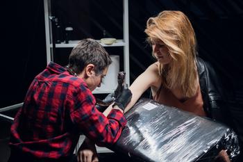 Profile view of tattoo artist tattooing a blonde woman’s arm