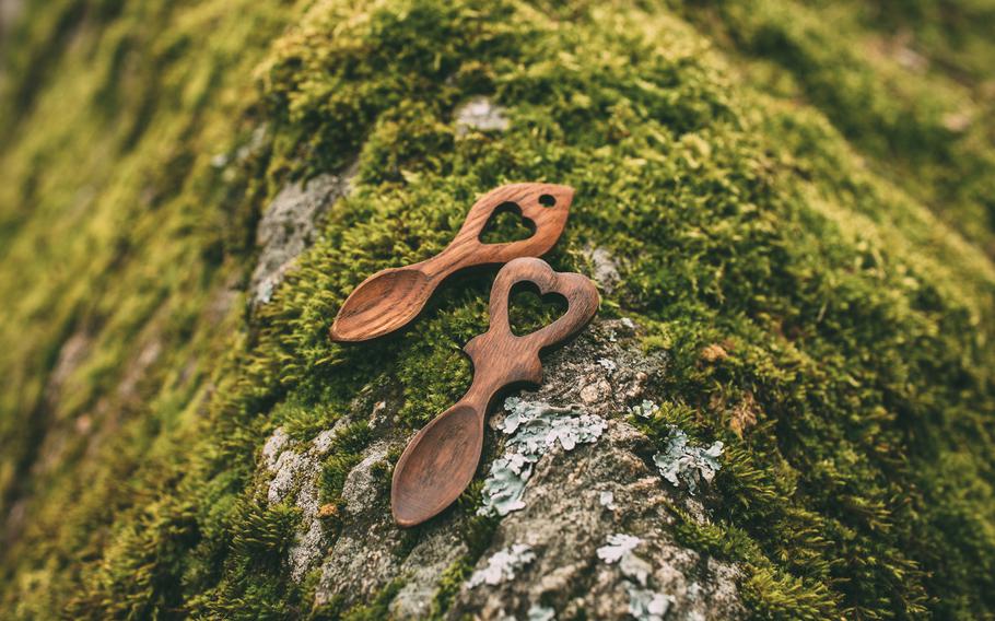 two wooden Welsh lovespoons sit on a mossy tree rot