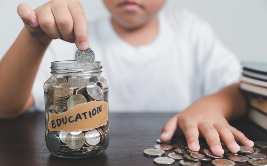 Boy putting coins into a clear jar labeled “EDUCATION.”