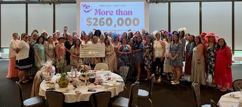 Wiesbaden Community Spouses’ Club luncheon, May 21, 2025 with participants standing behind a circular table and infront of a digital sign reading “More than$260,000”