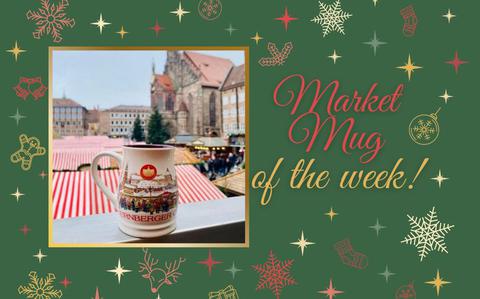 Photo Of An overview of the red and white pin-strip huts of the Nuremberg Christmas market. a cream-colored mug with a snowy city sits on the ledge.  