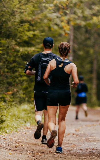 young man and woman running at forest trail 