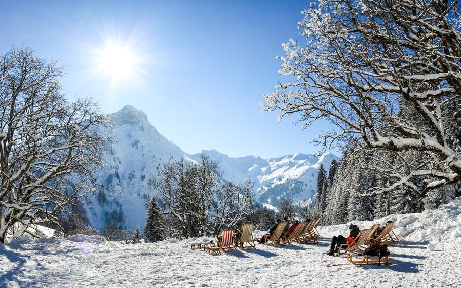 Group of people sitting with deck chairs in sunny winter mountains. Sunbathing in snow. Germany, Bavaria, Allgau, Schwarzenberghuette.