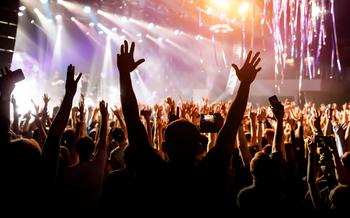 A man with his hands up at a concert of his favorite group. Light from the stage is illuminating the photo.