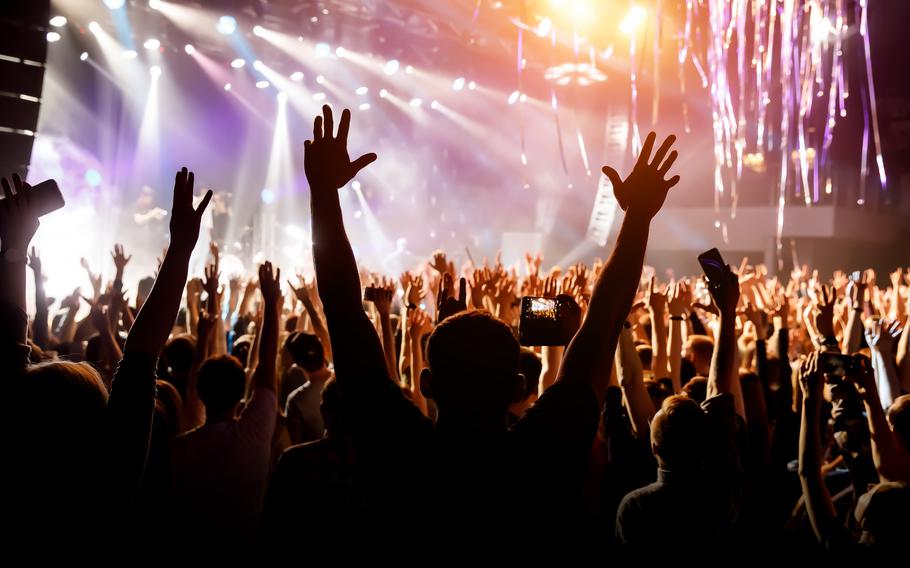 A man with his hands up at a concert of his favorite group. Light from the stage is illuminating the photo.